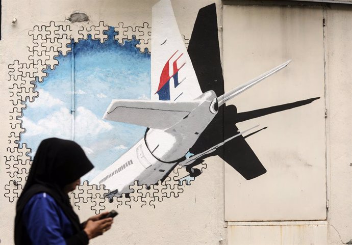 Archivo - March 7, 2019 - Shah Alam, Selangor, Malaysia - A pedestrian uses her smartphone while walk past a mural representing the missing Malaysia Airlines flight MH370 at an alley in Shah Alam. Flight MH370, which disappeared almost exactly five years 