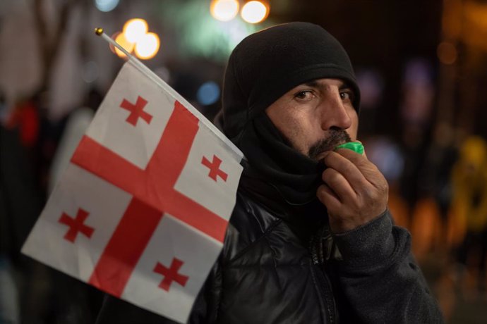 December 17, 2024, Tbilisi, Georgia: A protester holding the Georgian flag blows a whistle during a demonstration near the parliament building on a New Year's decorated street. A rally is staged near the parliament building, opposing the government's susp