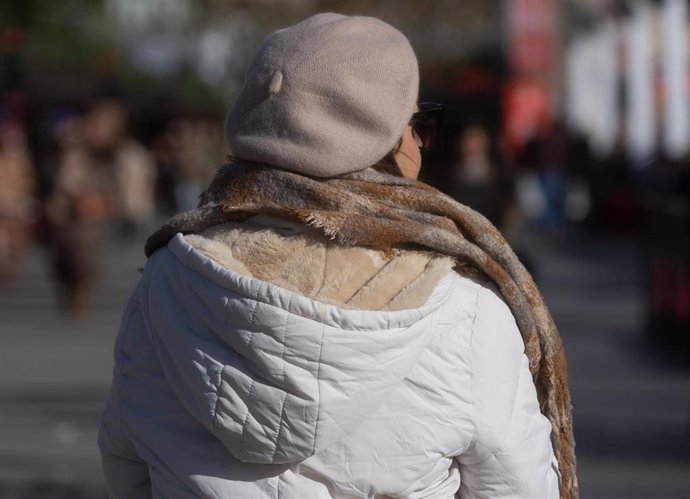 Una mujer abrigada con bufanda y gorro pasea por la calle. Imagen de archivo