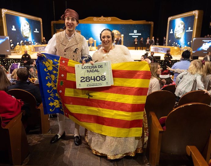 Una pareja vestidos con el traje de fallera y una bandera de la Comunidad Valenciana durante la celebración del Sorteo Extraordinario de la Lotería de Navidad 2024, en el Teatro Real, a 22 de diciembre de 2024, en Madrid (España). El Estado reparte hoy un