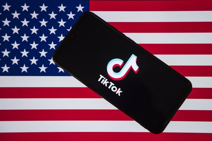 18 December 2024, India, ---: The TikTok logo is displayed on a mobile phone screen with US flag in the background. United States President-elect Donald Trump is to meet the CEO of TikTok, as the social media giant fights plans by US authorities to ban it