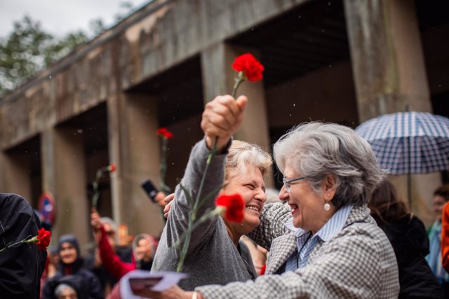 Dos mujeres se abrazan durante el acto conmemorativo por el 50 aniversario del 25 de Abril en Portugal, en la Plaza de la Música de Compostela, a 25 de abril de