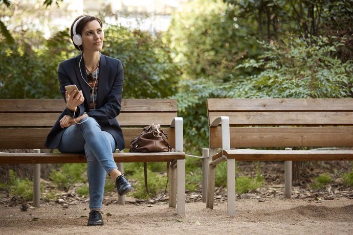 Archivo - Mujer escuchando música en el banco en el parque