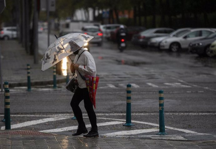 Archivo - Una mujer camina protegida de la lluvia con un paraguas.