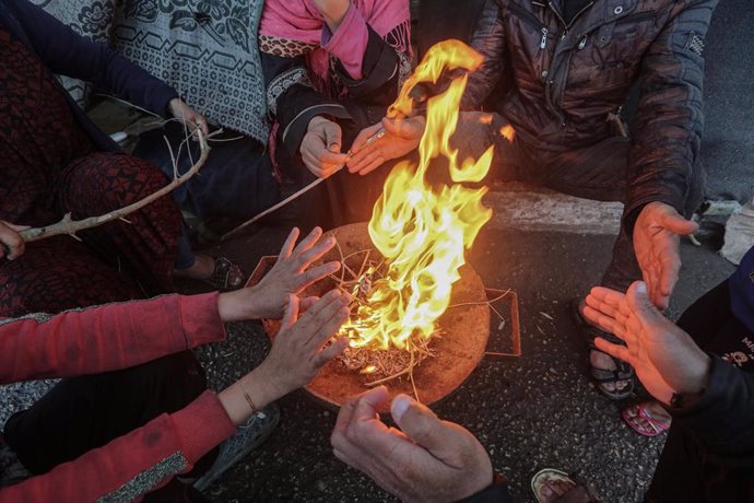 Desplazados palestinos se calientan con fuego en la Franja de Gaza