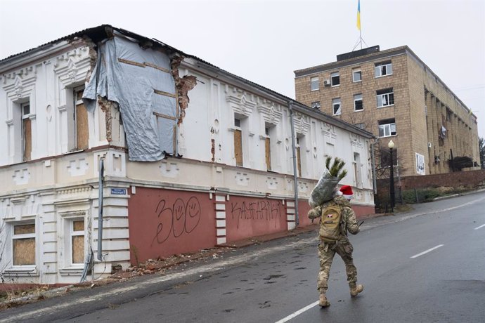 24 December 2024, Ukraine, Kupiansk: A Ukrainian soldier wearing a Santa hat carries a Christmas tree on Christmas Eve in Kupiansk, in eastern Kharkiv, which was badly destroyed by Russian artillery and drone attacks. Photo: Miguel Candela/SOPA Images via