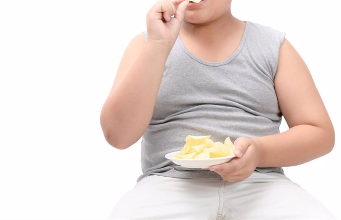 Archivo - Niño con sobrepeso comiendo patatas fritas.