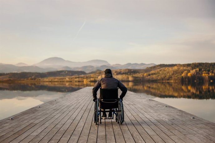 Archivo - Hombre discapacitado sentado en silla de ruedas en un embarcadero y admirando la naturaleza junto al lago