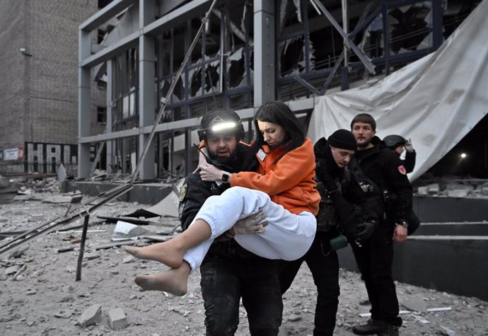 10 December 2024, Ukraine, Zaporizhzhia: A policeman carries a woman who was rescued from a building destroyed by a Russian missile attack in Zaporizhia in south-eastern Ukraine. 