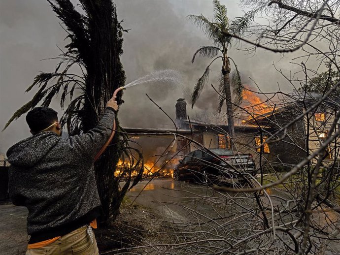 Un hombre utiliza una manguera de jardín en un incendio tras los feroces incendios en California