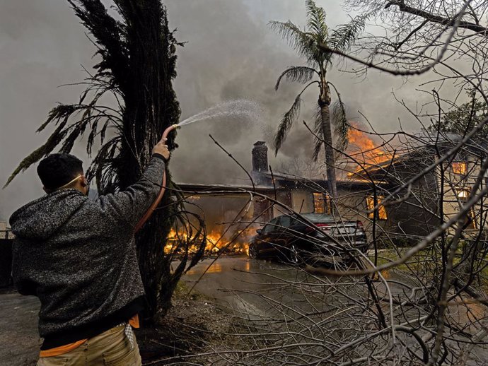 January 10, 2025, Altadina, California, USA: A man uses a garden hose on a fire  as businesses and properties were destroyed in the aftermath of the fierce Eaton fires on Wednesday, January 8, 2025, in Altadena, California. NICK UT/PI