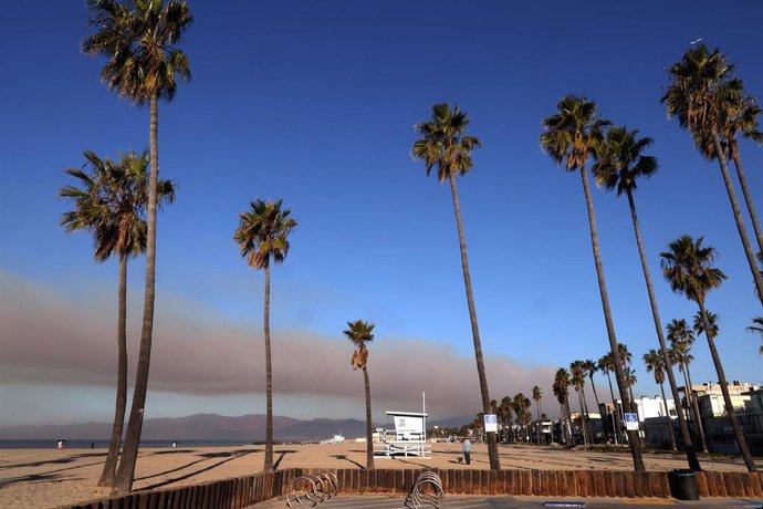 Un hombre pasea a su perro en Venice Beach mientras continúa ardiendo el incendio de Palisades