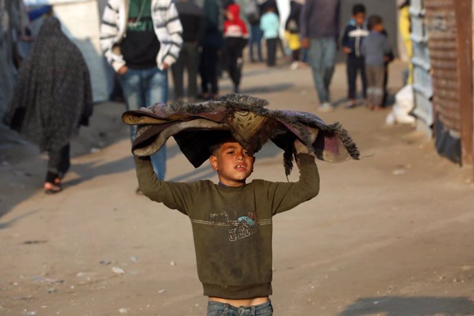 January 11, 2025, Deir Al-Balah, Gaza Strip, Palestinian Territory: A boy carries a folded rug on his head. Palestinians taking shelter in tent camps are battling harsh weather conditions as heavy rainfall has flooded their tents, in Deir al-Balah city. T