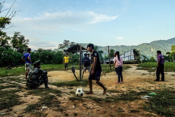 Archivo - Imagen de archivo de un soldado del KIA junto a varios niños que juegan al fútbol en el estado de Kachin, en el norte de Birmania.