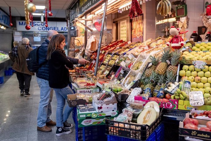 Varias personas hacen compras de última hora en un mercado.