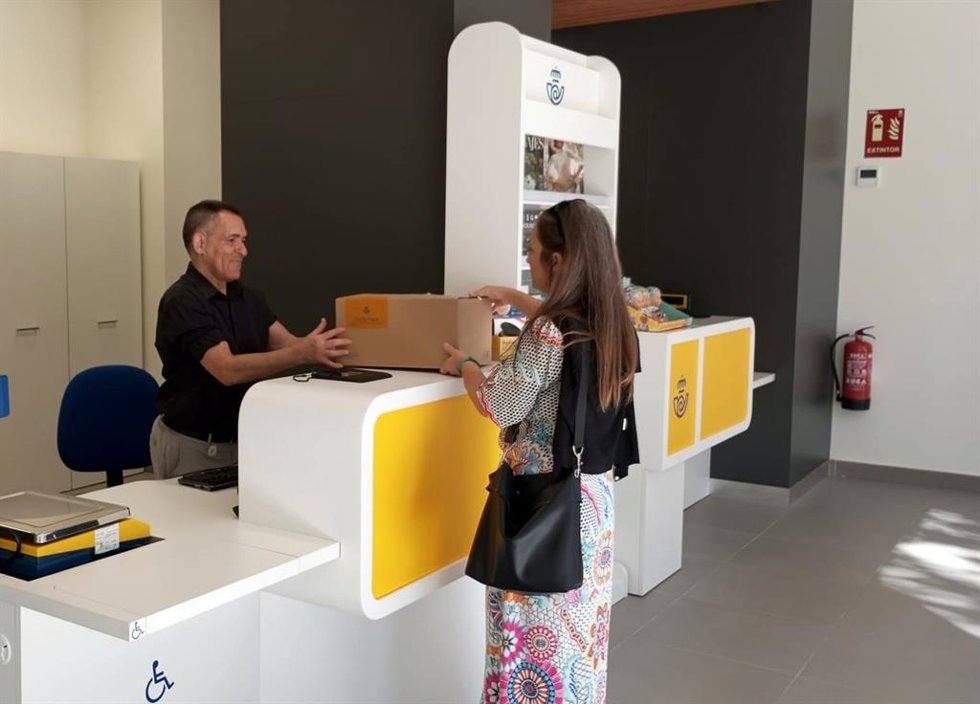 Archivo - Una ciudadana recoge un paquete en una oficina de Correos.