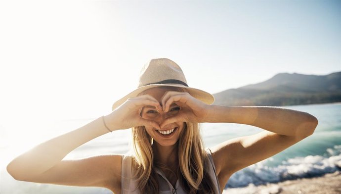 Archivo - Mujer sonriendo haciendo un corazón con las manos en la playa.