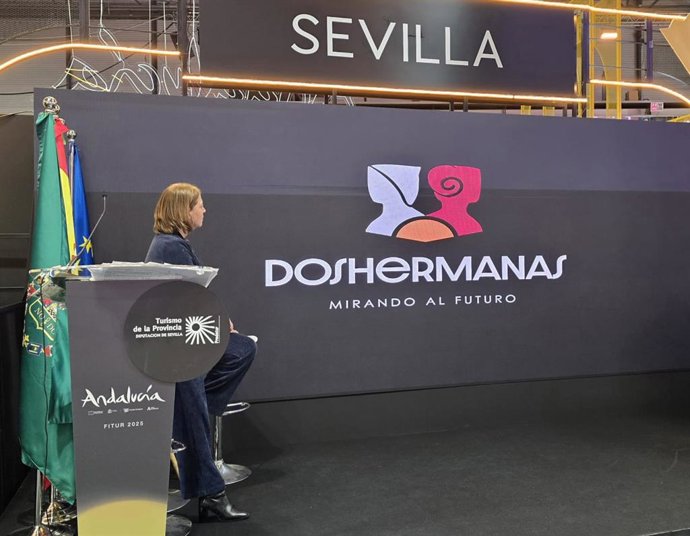 La periodista Mabel Mata, que ha conducido las presentaciones de municipios y empresas en el stand de la provincia, observa el logo de Dos Hermanas.