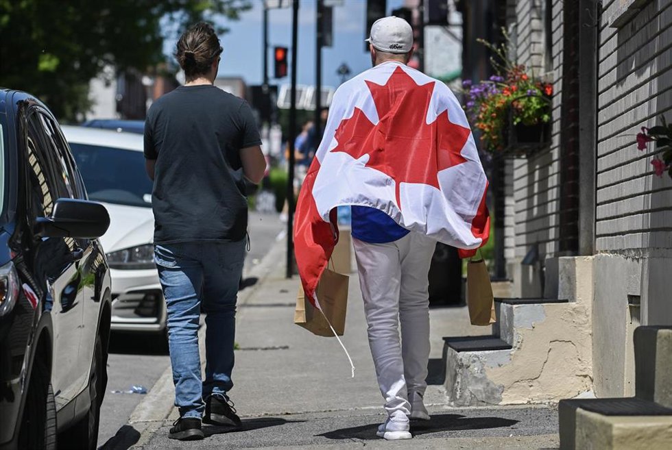 Archivo - Dos personas caminan por las calles de Montreal con una bandera de Canadá.
