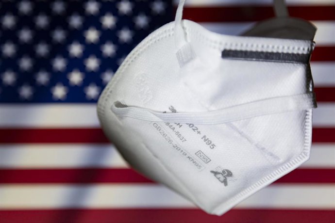 Archivo - Ilustración de una mascarilla y en el fondo la bandera de Estados Unidos