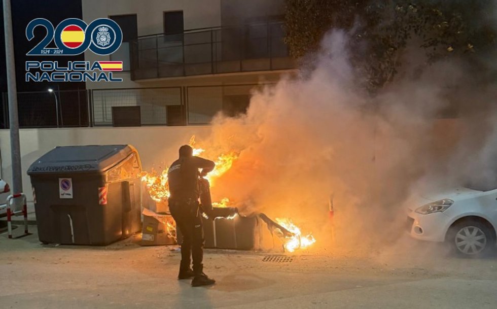 Un agente de la Policía trata de sofocar el incendio en un contenedor de basura con un extintor.