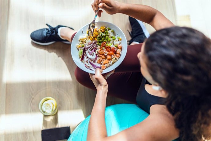 Archivo - Shot of sporty young woman eating healthy while listening to music sitting on the floor at home.