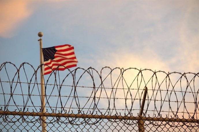 Archivo - FILED - 16 October 2018, Cuba, Guantanamo Bay: A US flag flies in the wind behind a barbed wire fence at the US prison camp in Guantanamo Bay. The United States has sent 11 Yemeni detainees of the notorious Guantanamo Bay prison to Oman, the Pen