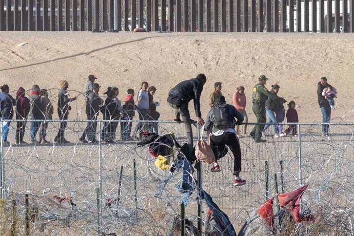 Archivo - 15 March 2024, US, Auburn Hills: Two men scale the cyclone fence installed by the Texas National Guard, as hundreds of migrants queue up along the border wall dividing Mexico and the United States, awaiting processing by the US Border Patrol. Ph