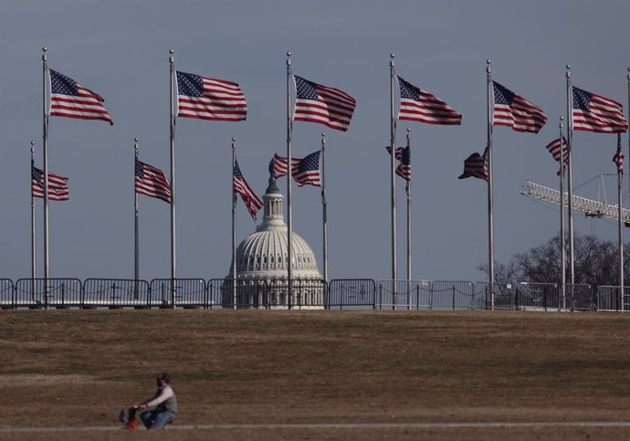 February 7, 2025, Washington Dc, Virginia, USA: A man rides a bicycle next to US flags on the Washington Monument platform with the US Capitol cupola in the background on February 7, 2025 in in Washington, DC.