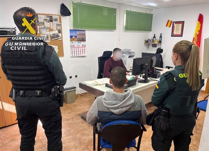 Uno de los detenidos sentado en una silla mientras es custodiado por varios agentes en una sala de un cuartel de la Guardia Civil