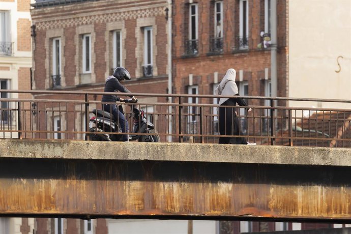 Archivo - Arquivo - 15 de fevereiro de 2024, Paris, França, França: Alfortville, França, 15 de fevereiro de 2024 - Uma mulher usando um hijab e um jovem em uma scooter atravessam uma ponte sobre o rio Marne, na região de Paris...ILUSTRAÇÃO, JEUNES FRANCAI