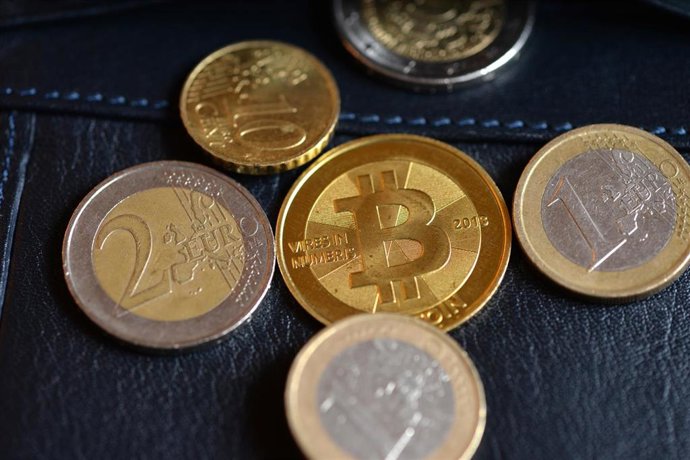 Archivo - FILED - 24 November 2013, Berlin: A Bitcoin and euro coins can be seen during the 'Bitcoin Exchange Berlin' at the Betahaus.