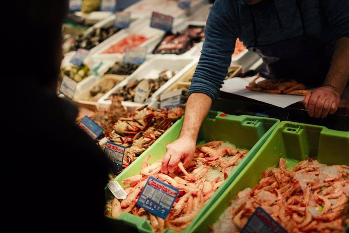 Archivo - Un tendero sirve langostinos a una mujer en un mercado