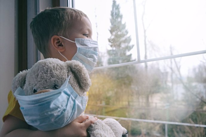 Archivo - Niño de enfermedad triste en cuarentena domiciliaria. El chico y su osito de peluche se sienta en el alféizar de la ventana y mira por la ventana. Protección del virus, pandemia de coronavirus, epidemia de prevención.