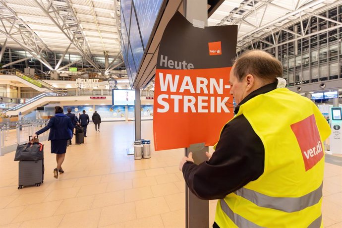 12 February 2025, Hamburg: A Verdi representative hangs up a poster reading "Warning strike" at Hamburg Airport. The employees of Flughafen Hamburg GmbH have been on warning strike since the night shift. Photo: Bodo Marks/dpa