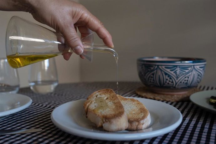 Archivo - Una persona echa aceite de una aceitera a una tostada.
