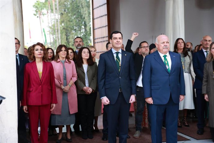 El presidente de la Junta, Juanma Moreno; el presidente del Parlamento, Jesús Aguirre; y la vicepresidenta y ministra de Hacienda, María Jesús Montero, siguen bajo la lluvia la interpretación del himno de Andalucía en el Parlamento por el 28F