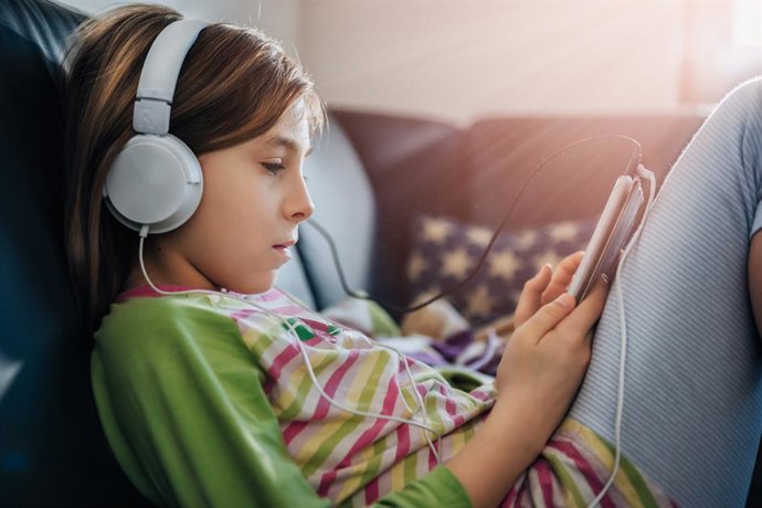 Archivo - Garota sentada em um sofá preto usando um tablet e ouvindo música