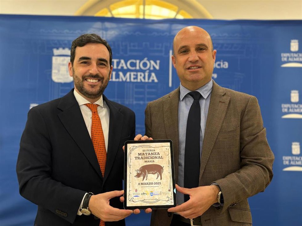 El diputado de Promoción Agroalimentaria, Comercio y Consumo de Almería, Carlos Sánchez, junto al vicepresidente de la Diputación de Almería y alcalde de María, José Antonio García, con el cartel de la Feria de la Matanza de María (Almería).