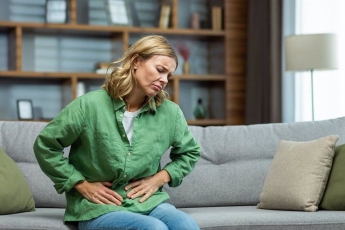 Archivo - Unhealthy senior woman sitting on sofa at home. Holding her stomach, grimacing in pain. She experiences severe abdominal pain, eating disorder, diarrhea, poisoning, menstruation, menopause.