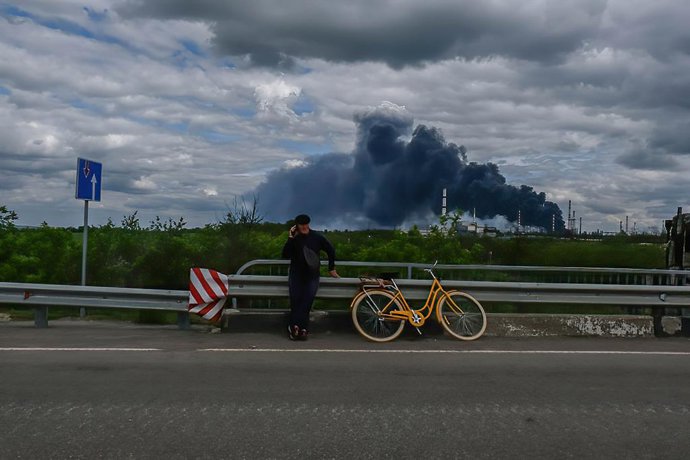 Archivo - Arquivo - 22 de maio de 2022, Lysycahans'k, Ucrânia: Um homem fala ao telefone com a refinaria de petróleo de Lysychansk em chamas ao fundo. Lysychansk é uma cidade alongada na margem direita alta do rio Donets, na região de Luhansk.