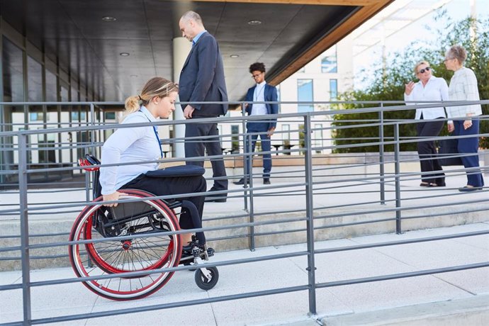 Archivo - Una mujer en silla de ruedas accede a un edificio público desde una rampa habilitada al respecto.