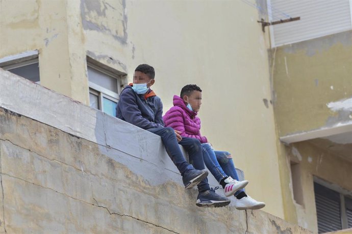 Archivo - Dos niños sentados sobre un muro en la nave de primera acogida del polígono del Tarajal, en una fotografía de archivo.