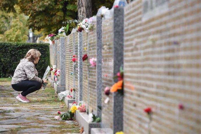 Archivo - Una mujer deja flores en la tumba de un ser querido.