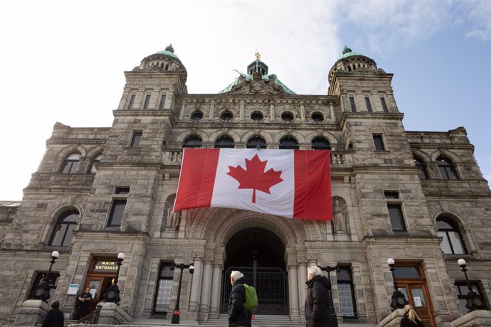 March 7, 2025, Victoria, Bc, CAN: A gigantic Canadian flag hangs over the ceremonial entrance at the legislature as people walk about in Victoria, B.C., on Friday, March 7, 2025.