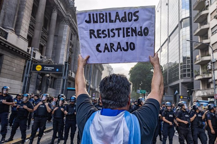 12 de março de 2025, Buenos Aires, Argentina: Um aposentado segura um cartaz expressando sua opinião durante a manifestação. No pedido de apoio aos aposentados, torcedores de futebol e ativistas entraram em confronto com a polícia ao redor do palácio legi