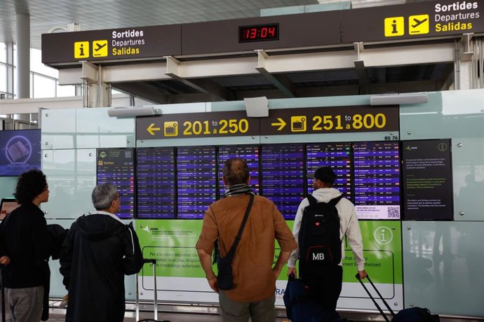 Archivo - Varias personas miran los paneles informativos en el aeropuerto de Barcelona-El Prat.