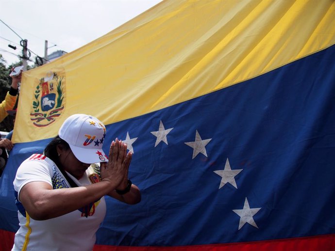 Archivo - January 9, 2025, Lima, Lima, Peru: Woman on her knees praying in front of a Venezuelan flag when hundreds of Venezuelans, responding to a worldwide call, took to the streets and gathered in front of the Venezuelan Embassy in Lima, carrying flags