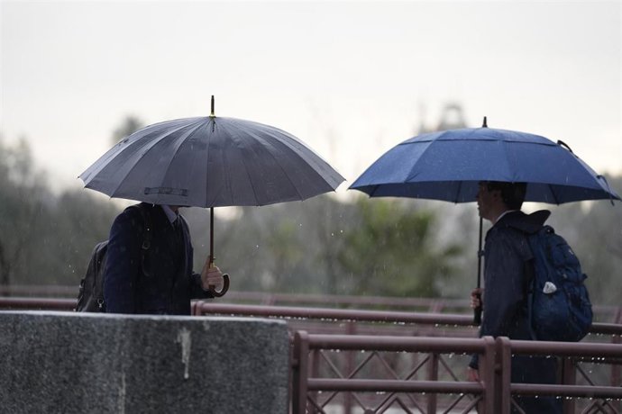 Varias se protegen de la lluvia con un paraguas.
