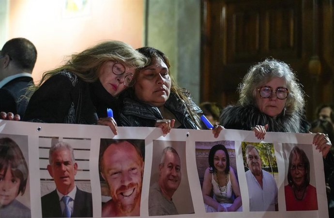 Archivo - Varias personas sostienen un cartel con imágenes de algunos fallecidos, durante una conmemoración por las víctimas de la DANA. 